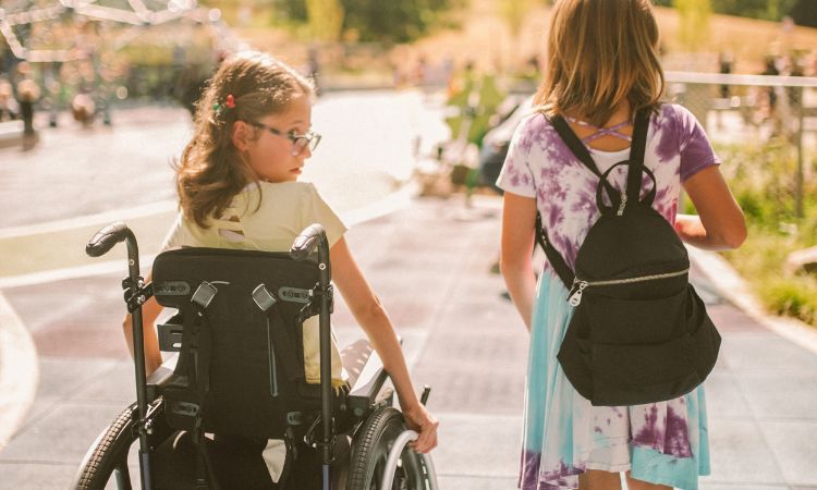 two girls getting ready to play, one is in a wheelchair, while her friend stands beside her